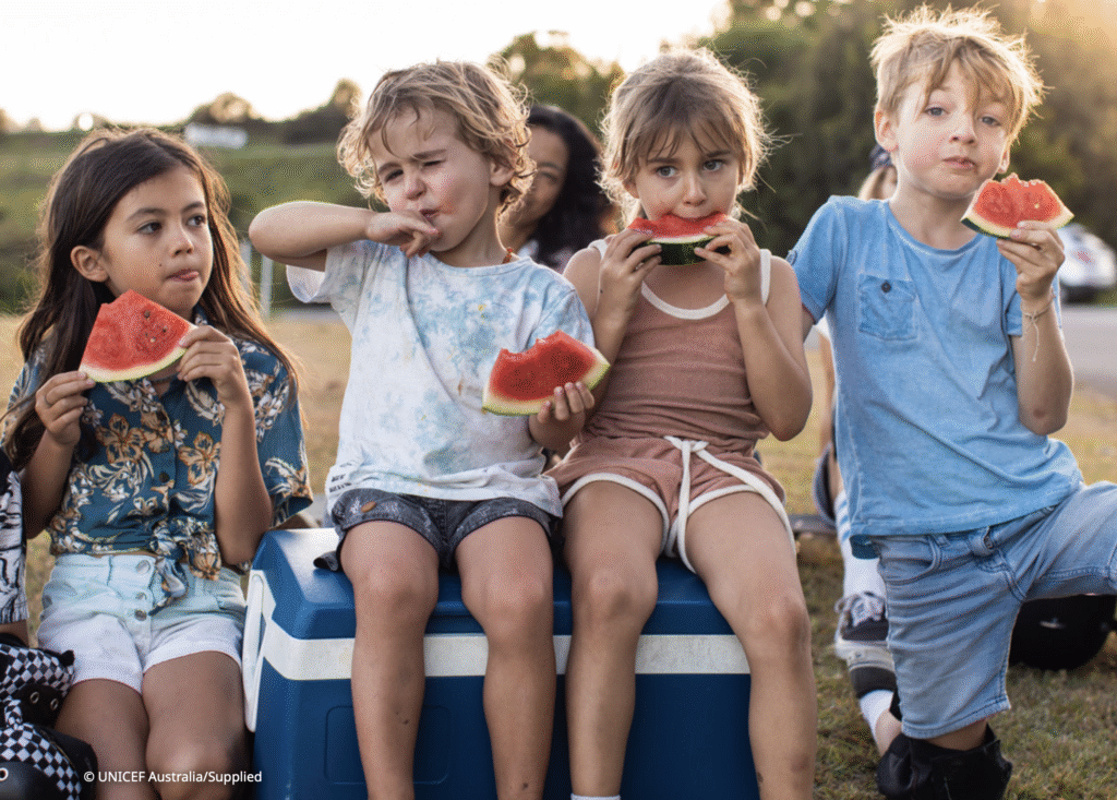 Four children sitting outdoors eating watermelon. Image from UNICEF from cover of the State of Australia's Children report.