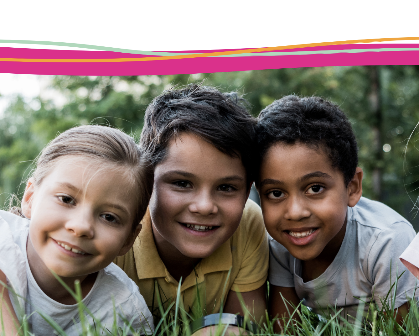 Three smiling children lying on grass, with a colourful stripe across the top of the image.