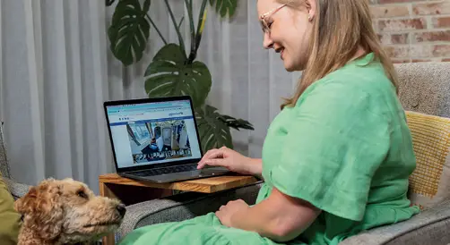 Lady in a green dress filling in the survey on her laptop with her dog by her side